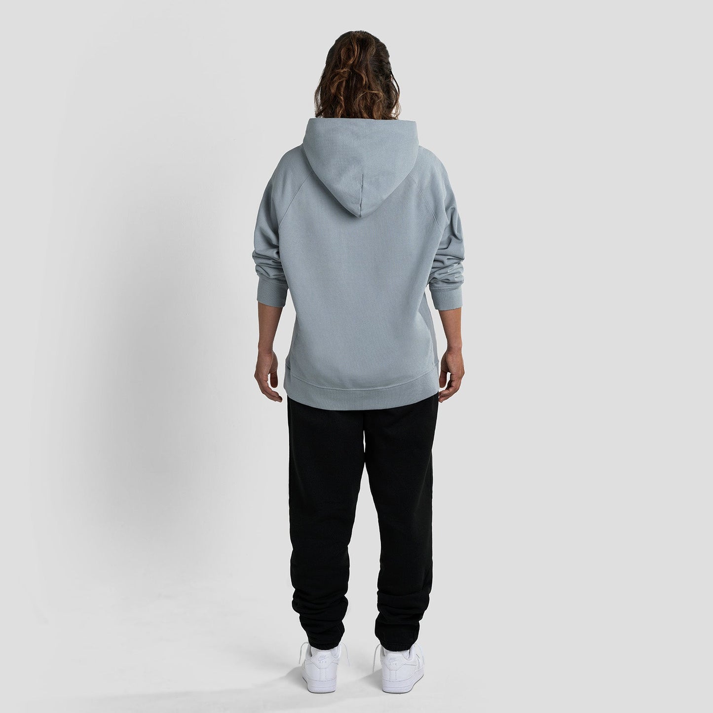 Person wearing a gray hoodie and black pants on a white background